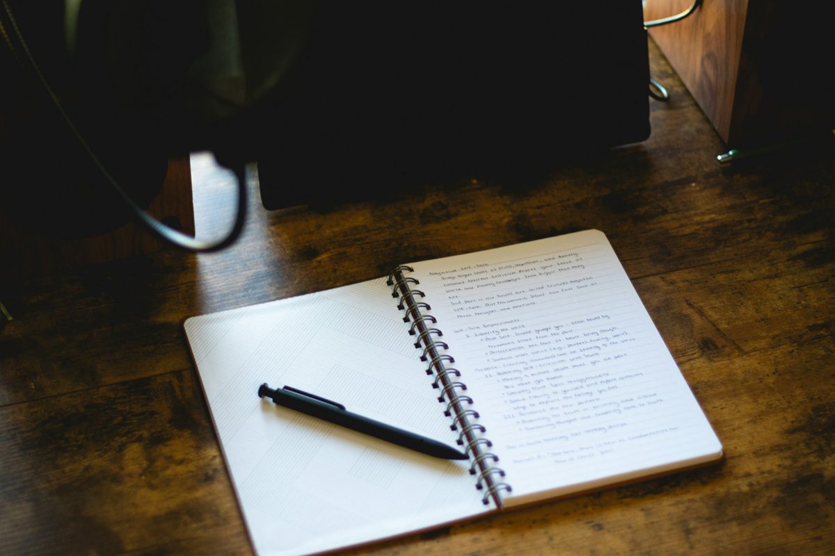 An open notebook with handwritten notes and a pen on a wooden desk